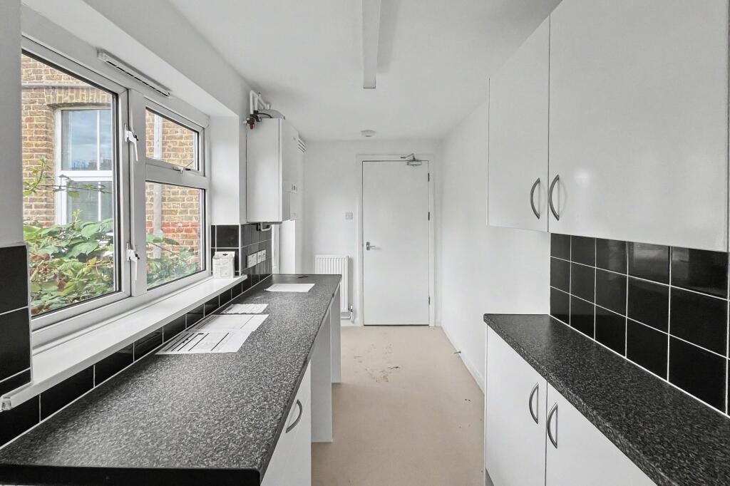 Narrow galley kitchen at 15 Arnold Road with white units, black tiled splashback and an old wall boiler