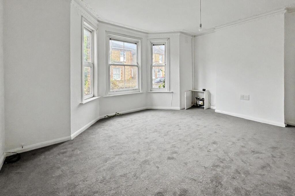 Empty lounge at 15 Arnold Road with a three-window bay, grey carpet and white walls