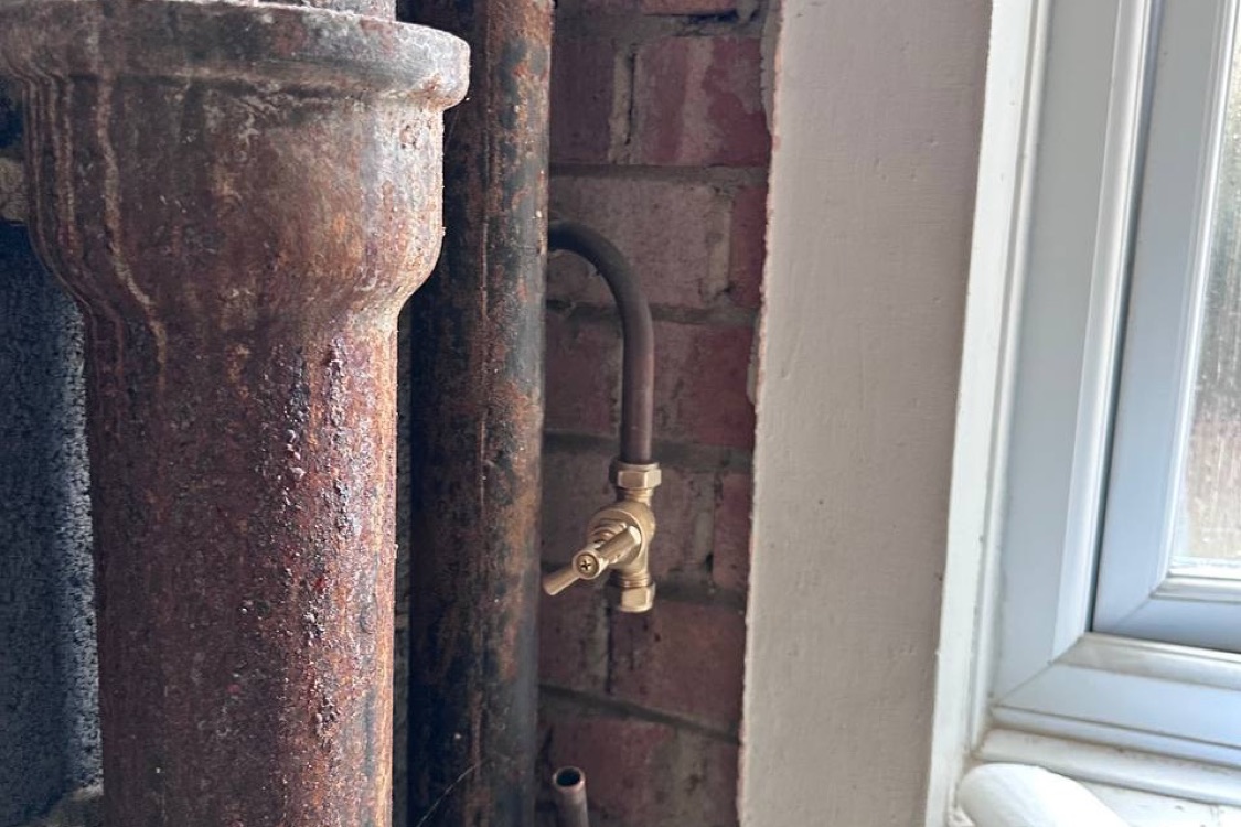 New brass cold water isolation valve fitted on a copper pipe against exposed brickwork, next to the old cast iron soil stack at the Innes Gardens flat