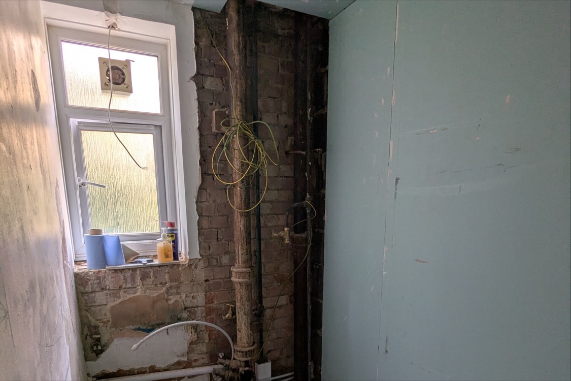 Second bathroom at the Innes Gardens flat with new stud wall lined in moisture-resistant board, exposed brick and old cast iron soil stack beside the window