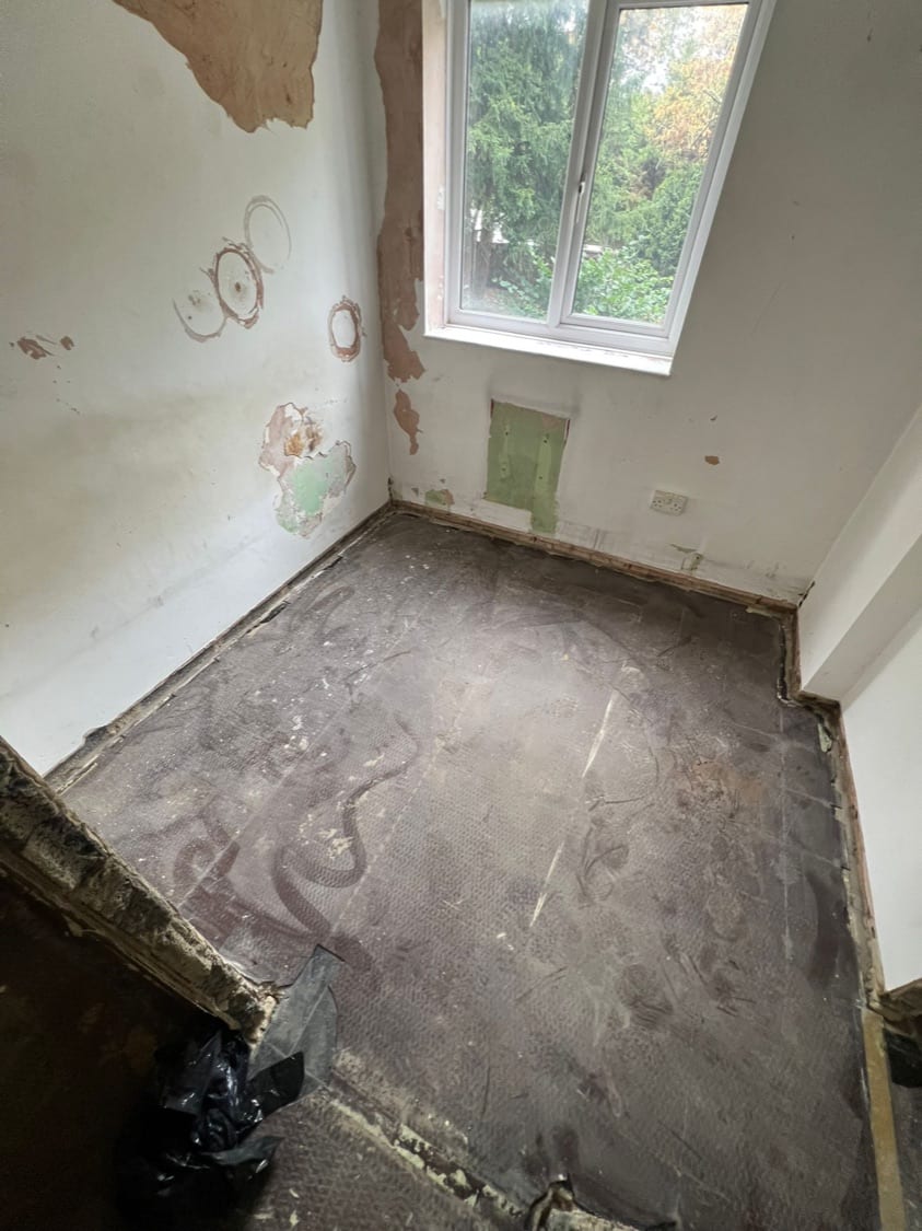 Bedroom stripped to bare floor and plaster, showing damp staining on the wall at the Innes Gardens flat